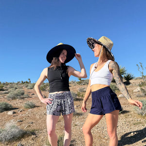 Two women wearing Ocean Wave navy shorts with straw hats — boho navy shorts back view