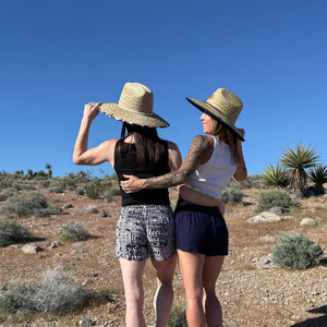 Back view of two women in ocean wave shorts with straw hats — Ember Glyph boho shorts