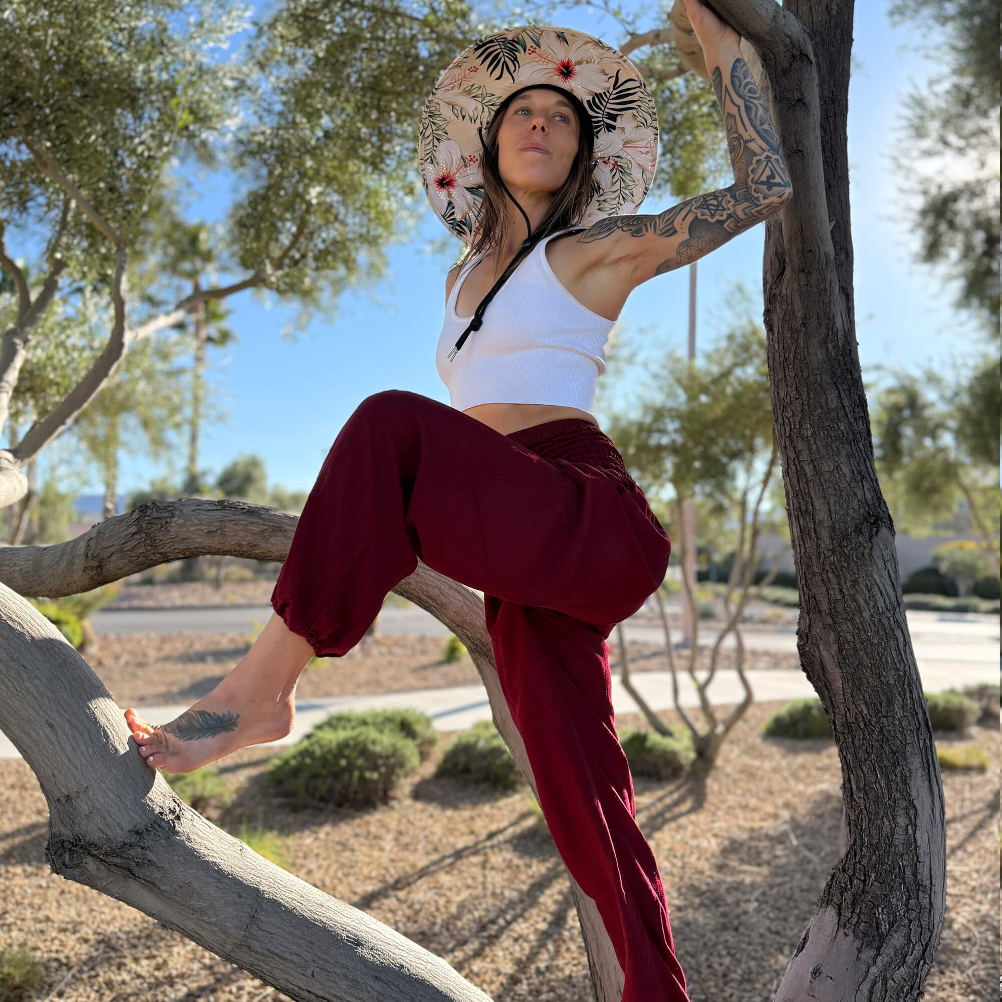 Karlene wearing The Layla Hollow Mat hat with Ruby Garnet harem pants by a tree — tropical floral sun hat
