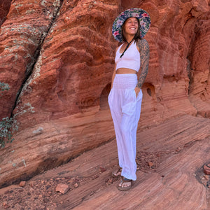 Karlene in The Tenley Rush & Mat hat and white harem pants outdoors — pink hibiscus boho straw hat