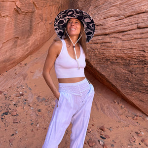 Karlene wearing The Ashley Rush & Mat straw hat with white harem pants — navy abstract circle sun hat