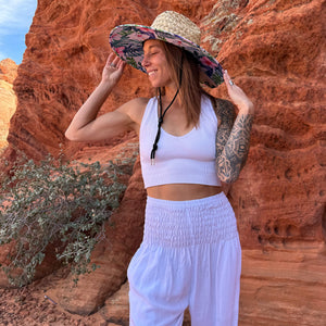 Karlene wearing The Tenley Rush & Mat hat with white harem pants — tropical hibiscus wide brim sun hat