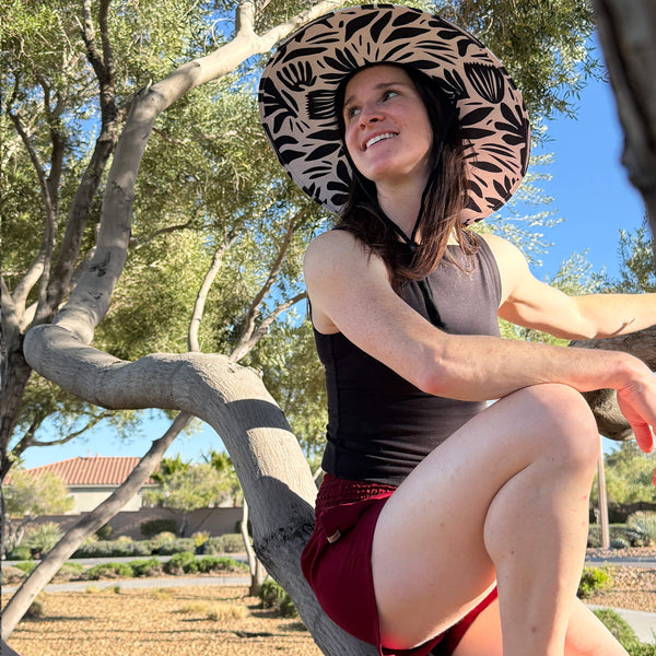 Woman wearing Ruby Garnet shorts by a tree with straw hat — red boho shorts women